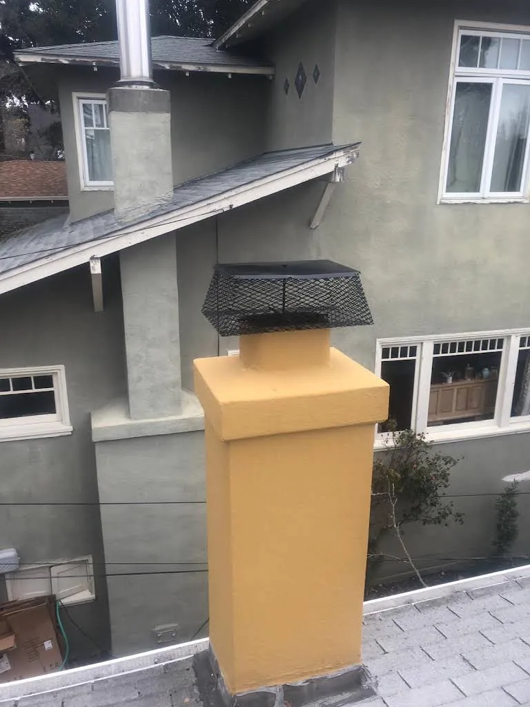 New black chimney cap installed on a tan stucco residential chimney
